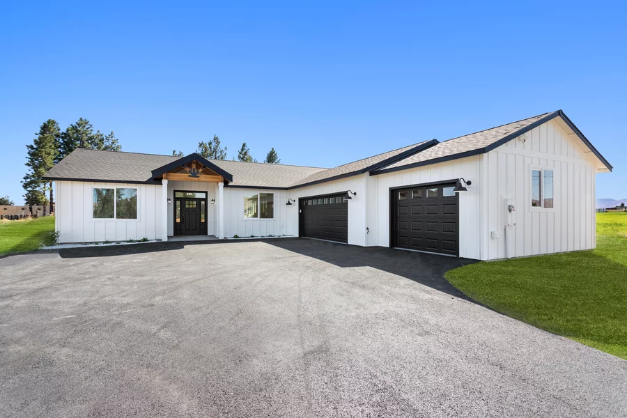 White modern farmhouse ranch home with black garage doors and a cedar gable entry.